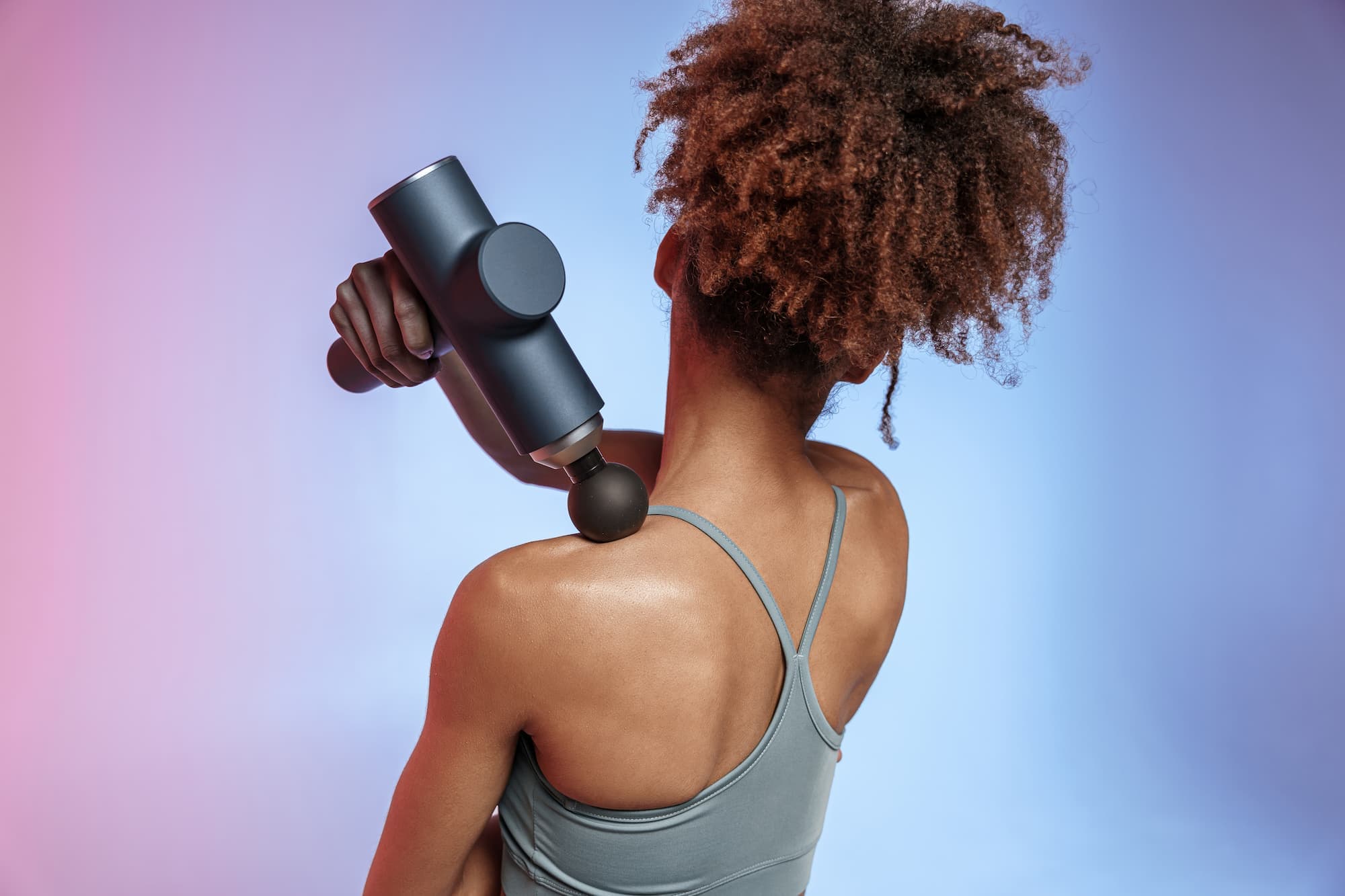 femme de dos utilisant un pistolet de massage pour libérer des tensions